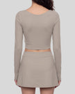 Mid body back view of a model wearing TrackLine Synergy Long-Sleeve Top in gray purple with a diagonal misty purple accent band and a matching gray purple wrap-style mini skirt