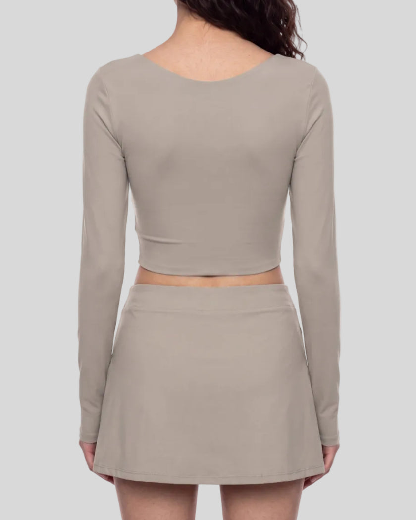 Mid body back view of a model wearing TrackLine Synergy Long-Sleeve Top in gray purple with a diagonal misty purple accent band and a matching gray purple wrap-style mini skirt