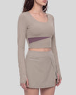 Mid body front angled view of a model wearing TrackLine Synergy Long-Sleeve Top in gray purple with a diagonal misty purple accent band and a matching gray purple wrap-style mini skirt