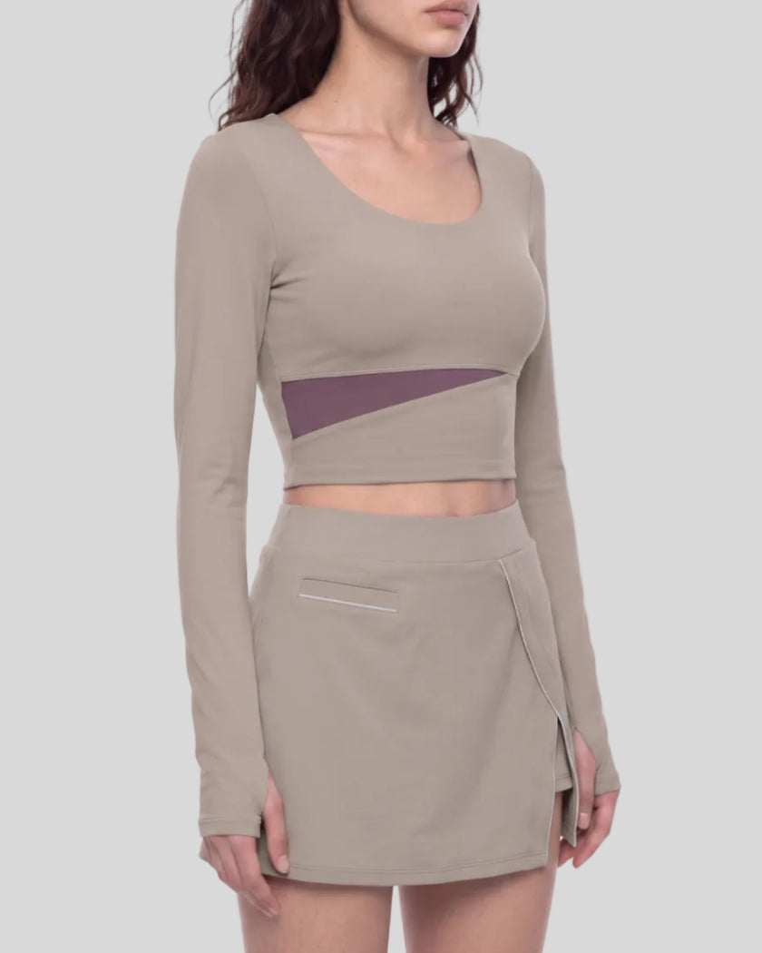 Mid body front angled view of a model wearing TrackLine Synergy Long-Sleeve Top in gray purple with a diagonal misty purple accent band and a matching gray purple wrap-style mini skirt