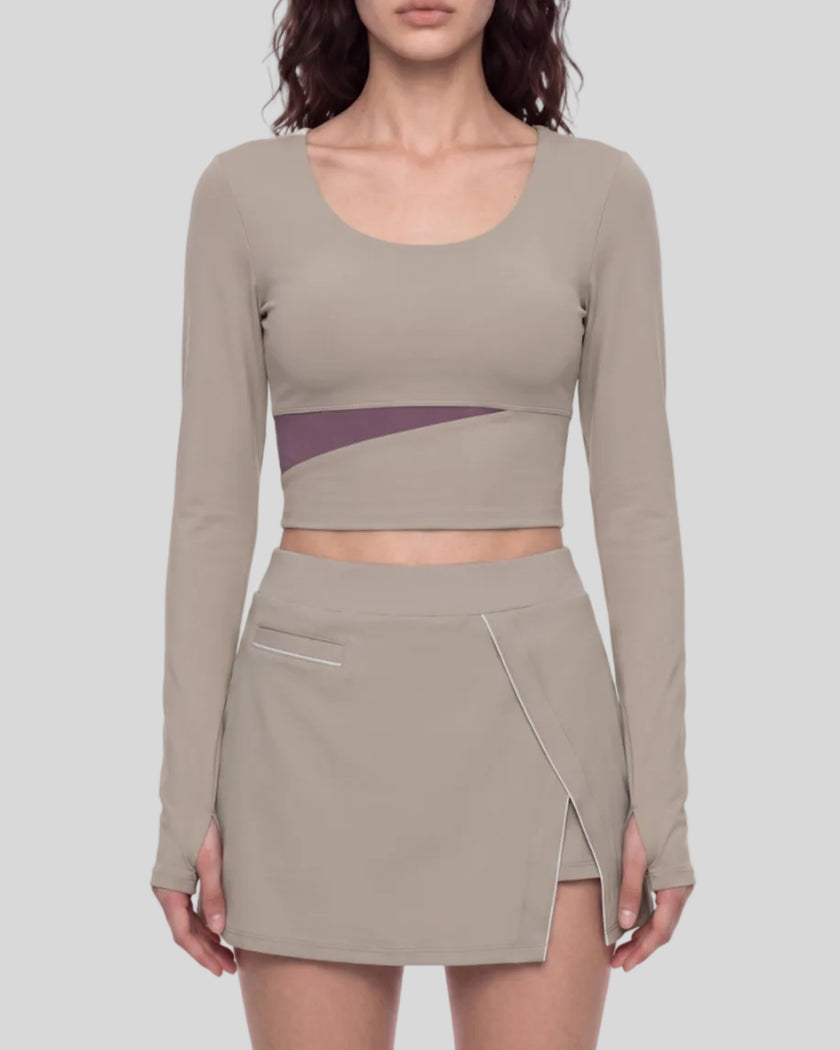 Mid body front view of a model wearing TrackLine Synergy Long-Sleeve Top in gray purple with a diagonal misty purple accent band and a matching gray purple wrap-style mini skirt