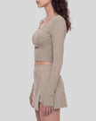 Mid body left side view of a model wearing TrackLine Synergy Long-Sleeve Top in gray purple with a diagonal misty purple accent band and a matching gray purple wrap-style mini skirt