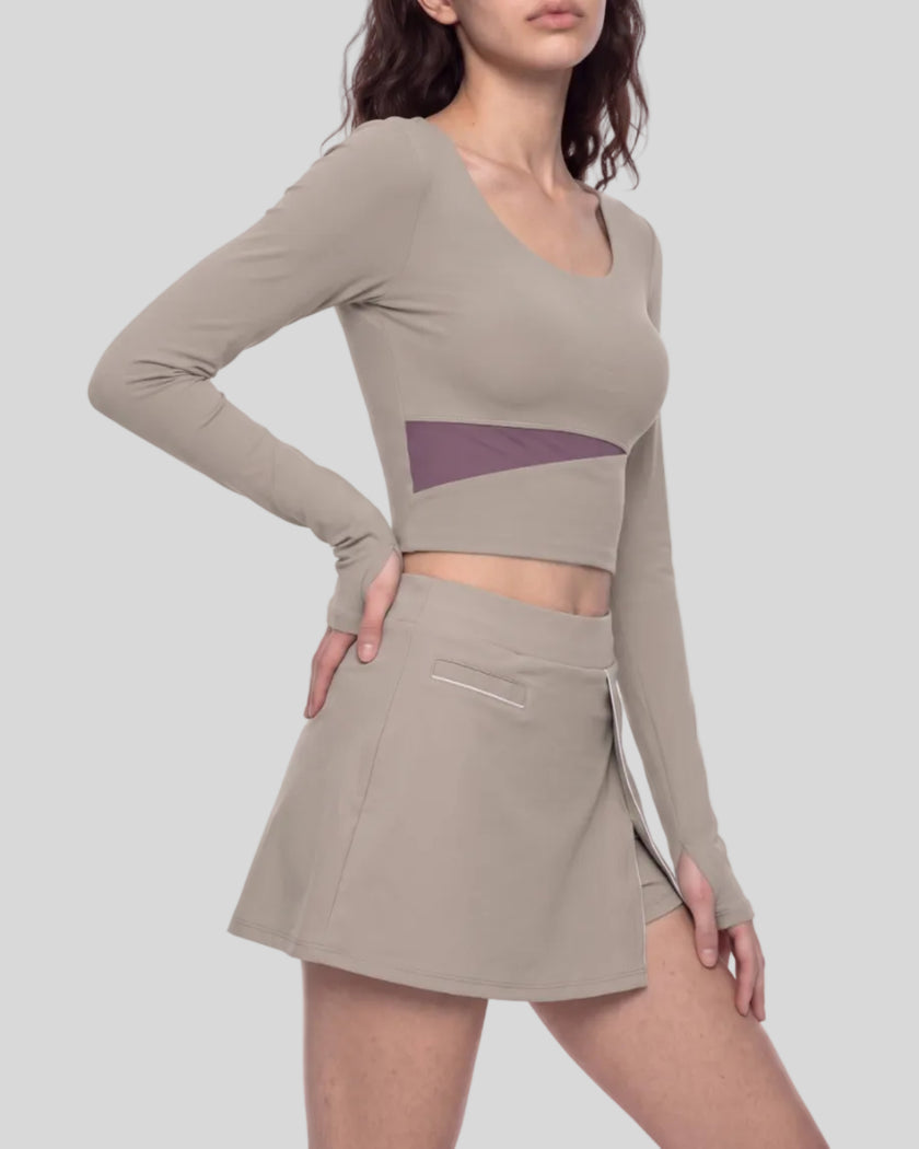 Mid body right side view of a model wearing TrackLine Synergy Long-Sleeve Top in gray purple with a diagonal misty purple accent band and a matching gray purple wrap-style mini skirt