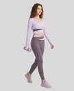 Full body view of woman wearing TrackLine Synergy Long Sleeve Top in light purple with deep purple color-block detail