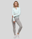Full body view of a woman modeling a light blue with light gray TrackLine Synergy Performance Jacket with matching leggings.