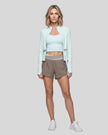 Full body view of a woman modeling a light blue with light gray TrackLine Synergy Performance Jacket with matching tank top and shorts.