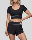 A woman modeling a black and dak gray TrackLine Synergy Performance Shorts with a matching sports top.