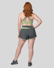 Woman wearing TrackLine Synergy Performance Shorts in Dark Gray with Bean Green waistband, back view