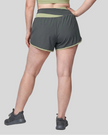 Woman wearing TrackLine Synergy Performance Shorts in Dark Gray with Bean Green waistband, lower body back view
