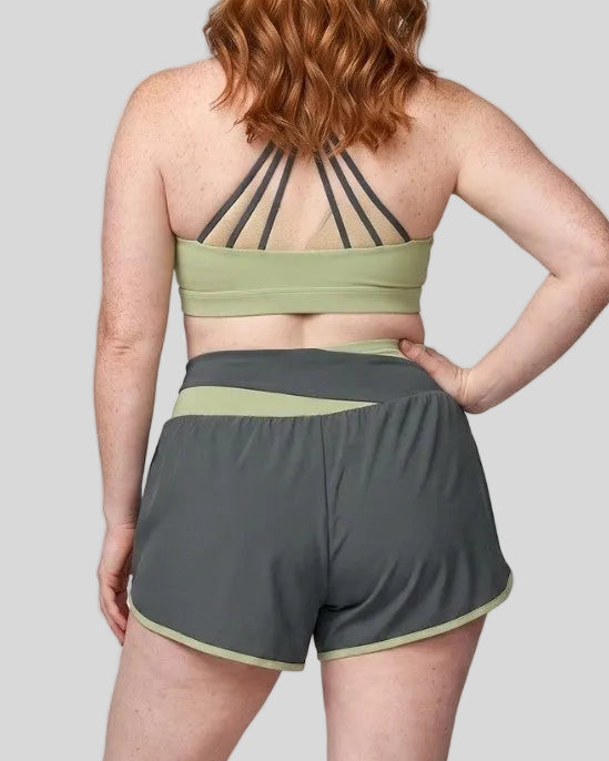 Back view of a woman modeling a dark gray and green bean TrackLine Synergy Performance Shorts with a matching sports bra.