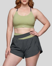 A woman modeling a dark gray and green bean TrackLine Synergy Performance Shorts with a matching sports bra.