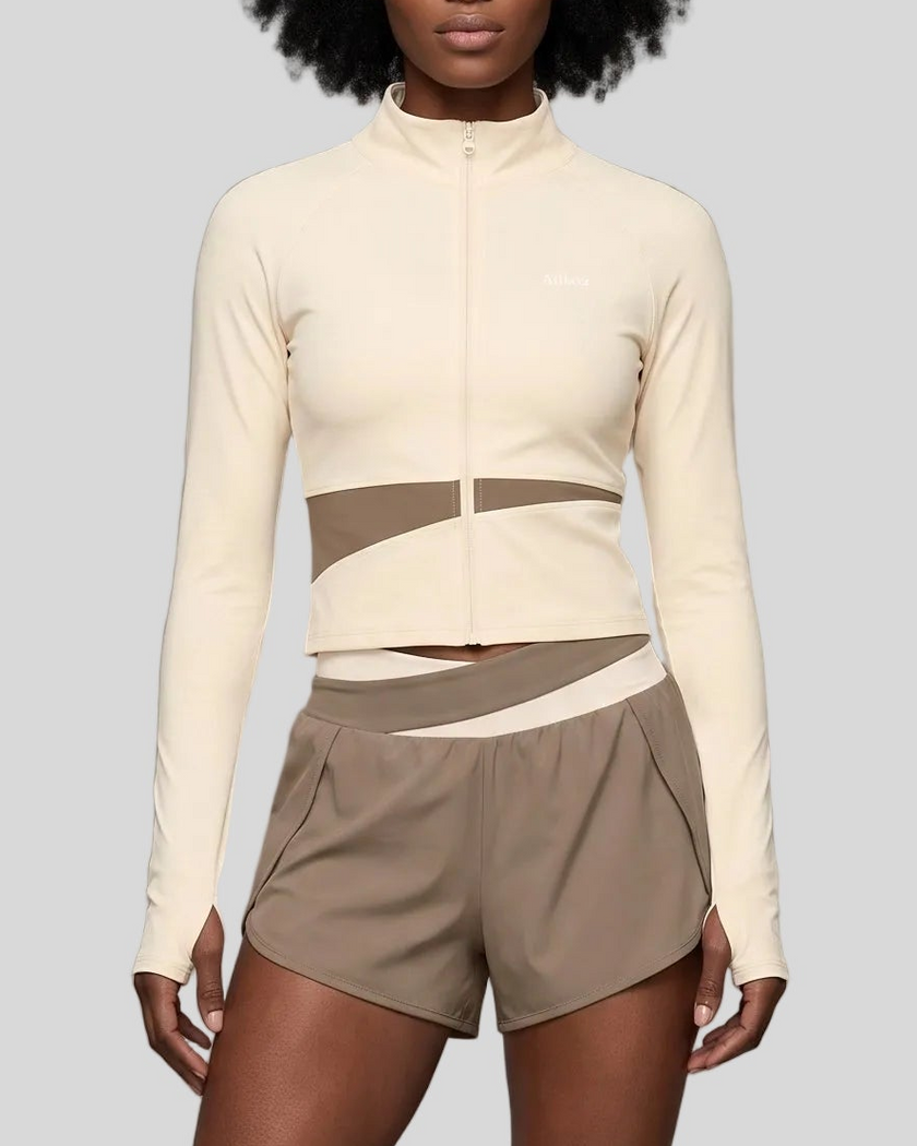 A woman modeling a light coffee and apricot TrackLine Synergy Performance Shorts with a matching sports jacket.