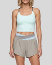 A woman modeling a light gray and light blue TrackLine Synergy Performance Shorts with a matching sports bra.