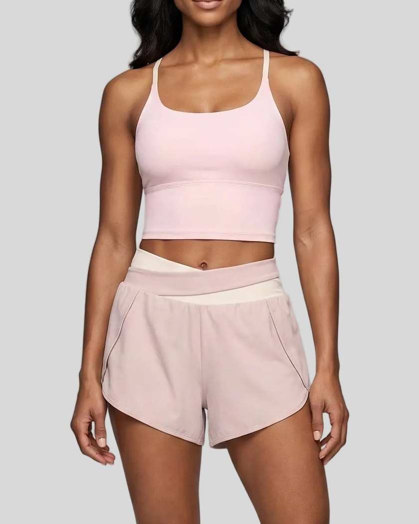 A woman modeling a light pink and apricot TrackLine Synergy Performance Shorts with a matching tank top.