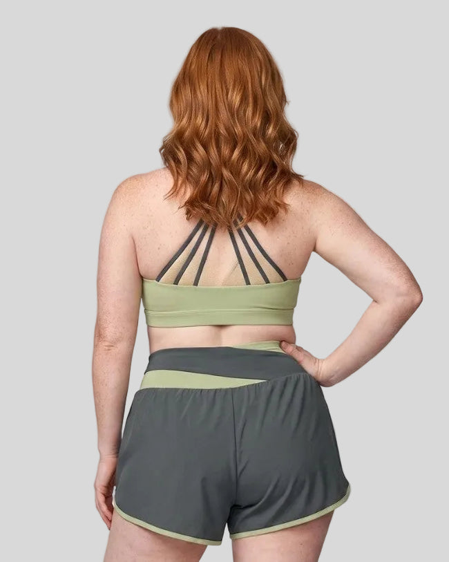 Woman wearing TrackLine Synergy Strappy Sports Bra in Bean Green with Dark Gray, mid-body back view showing multi-strap detail