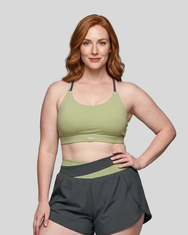 Woman wearing TrackLine Synergy Strappy Sports Bra in Bean Green with Dark Gray, mid-body front view