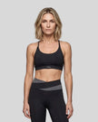 Woman wearing TrackLine Synergy Strappy Sports Bra in Black, mid-body front view