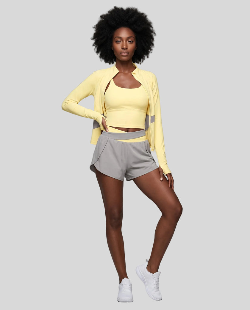 Woman modeling a Light Yellow with Light Gray TrackLine Synergy Tank Top with matching shorts and jacket, paired with white sneakers.