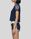 Mid body side view of the Athlesi TrackLine Track Shorts in blue paired with the TrackLine Varsity Tee