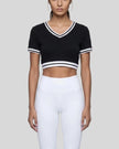 Mid body front view of the Athlesi TrackLine V-Neck Crop Tee in black styled in a minimalist modern setting