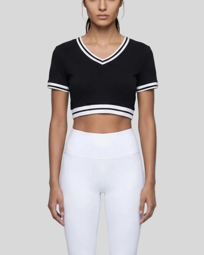 Mid body front view of the Athlesi TrackLine V-Neck Crop Tee in black styled in a minimalist modern setting