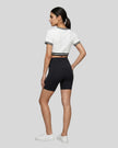 Full body back view of the Athlesi TrackLine V-Neck Crop Tee in white in a minimalist editorial setting