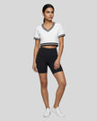 Full body front view of a woman wearing the Athlesi TrackLine V-Neck Crop Tee in white styled with modern athleisure pieces