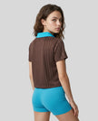 Back angle view of a woman wearing the Athlesi TrackLine Varsity Jersey in brown and blue
