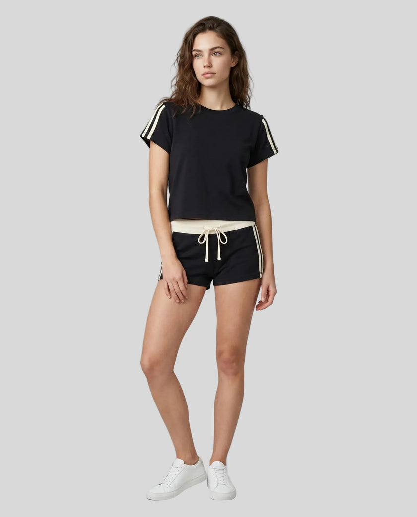 Full body front view of a woman wearing the Athlesi TrackLine Varsity Tee in black styled with matching TrackLine Track Shorts