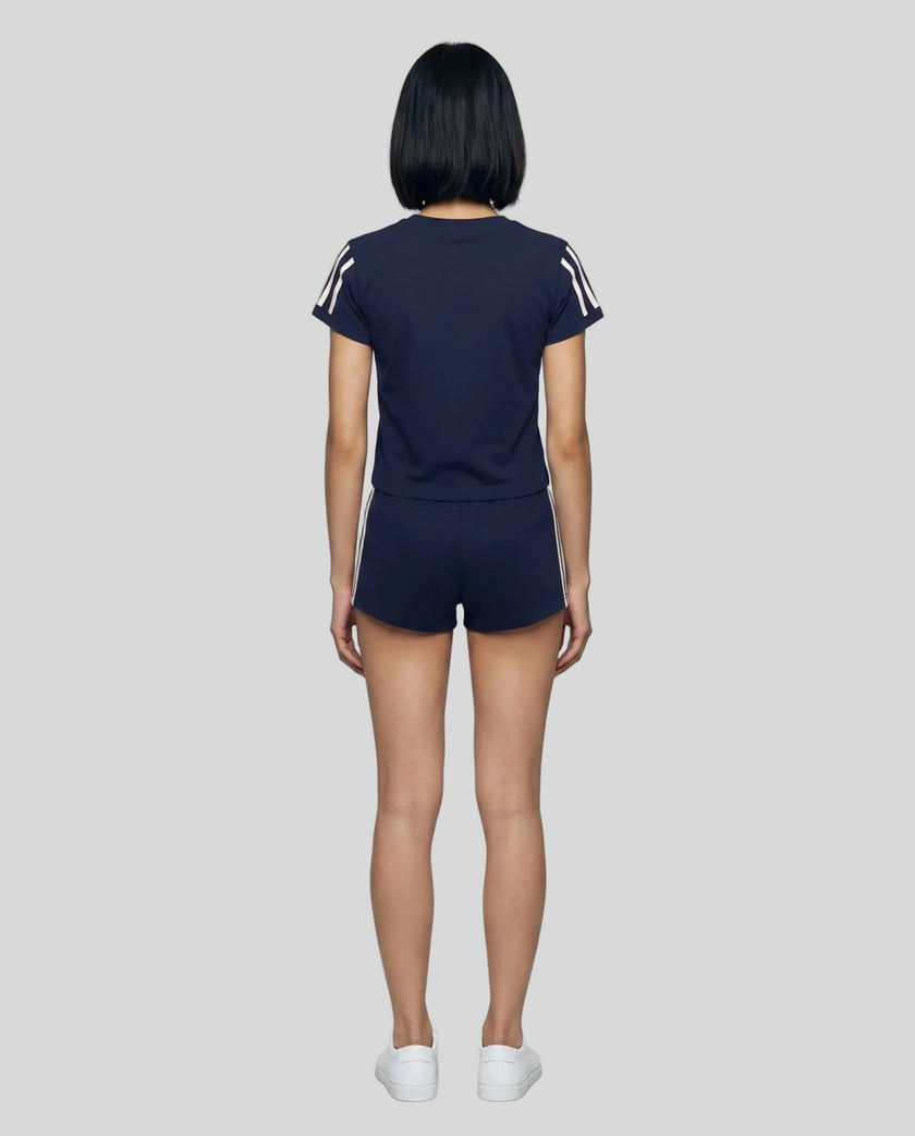 Full body back view of the Athlesi TrackLine Varsity Tee in blue in a clean modern architectural environment