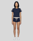 Full body front view of a woman wearing the Athlesi TrackLine Varsity Tee in blue styled with matching TrackLine Track Shorts