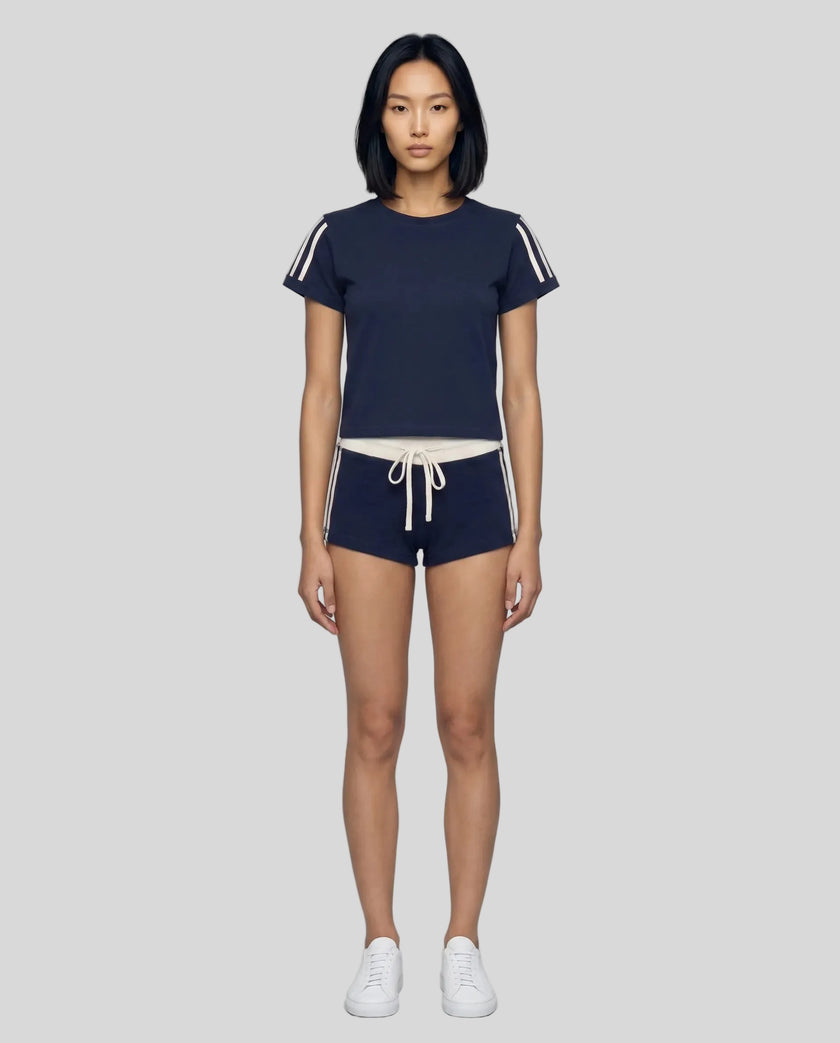 Full body front view of a woman wearing the Athlesi TrackLine Varsity Tee in blue styled with matching TrackLine Track Shorts