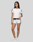 Full body front view of a woman wearing the Athlesi TrackLine Varsity Tee in white styled with matching TrackLine Track Shorts