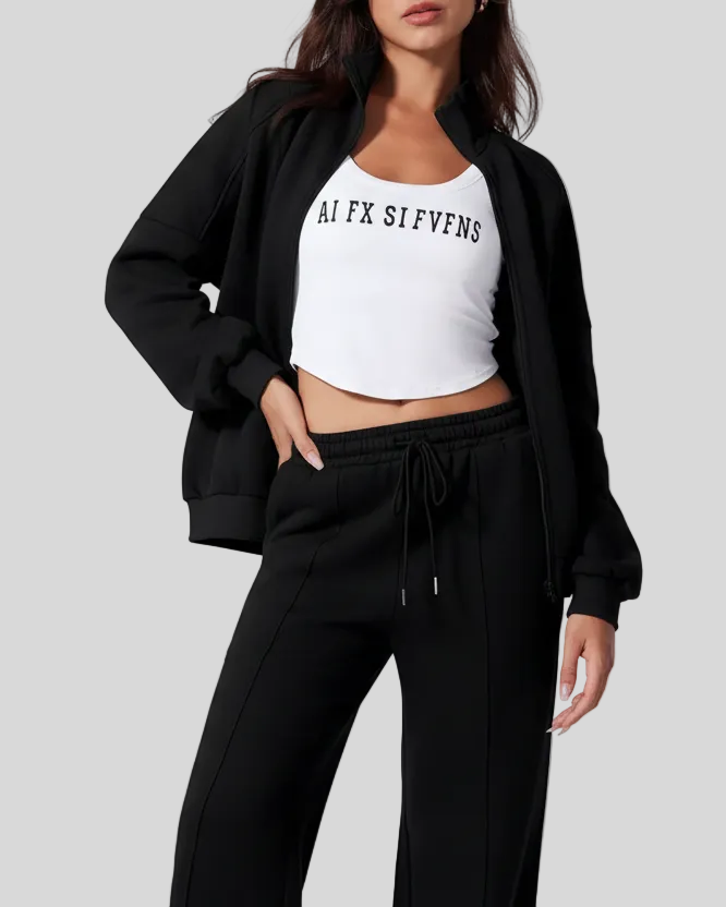 Woman wearing a black tracksuit with a white crop top on a light gray background